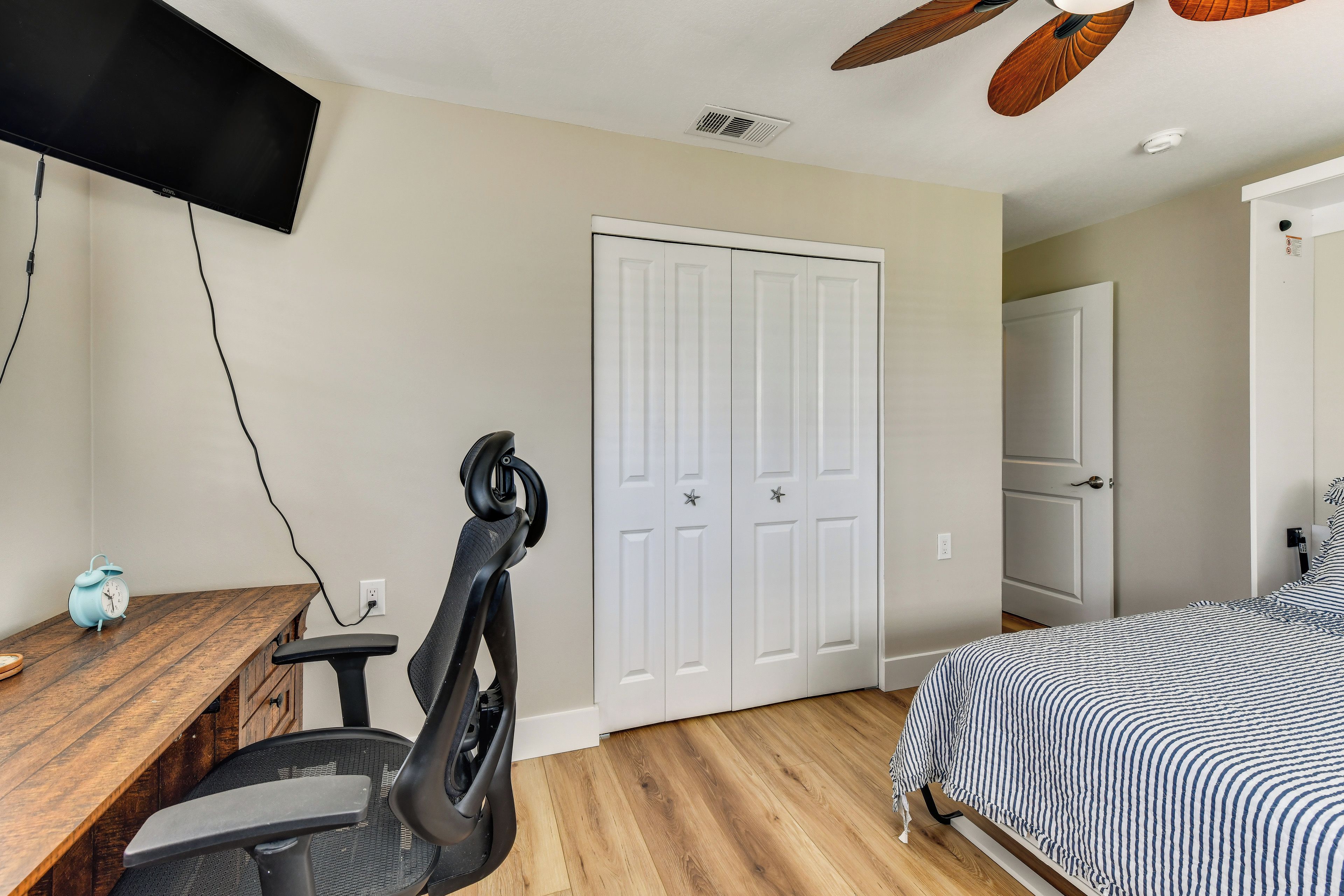 A bedroom with a bed, a desk with a chair, a television mounted on the wall, and a door with a star decoration.