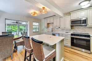 A modern kitchen with white cabinetry, a central island, and a dining area with wicker chairs. - Canal-front Gem w/ Dock & Guest Home in Cortez! (Cortez)