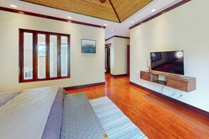 A modern bedroom with a large bed, a television mounted on a wooden cabinet, and a window with blinds.