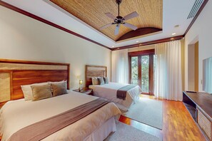 A bedroom with two beds, a ceiling fan, and a view of the outdoors through large windows.