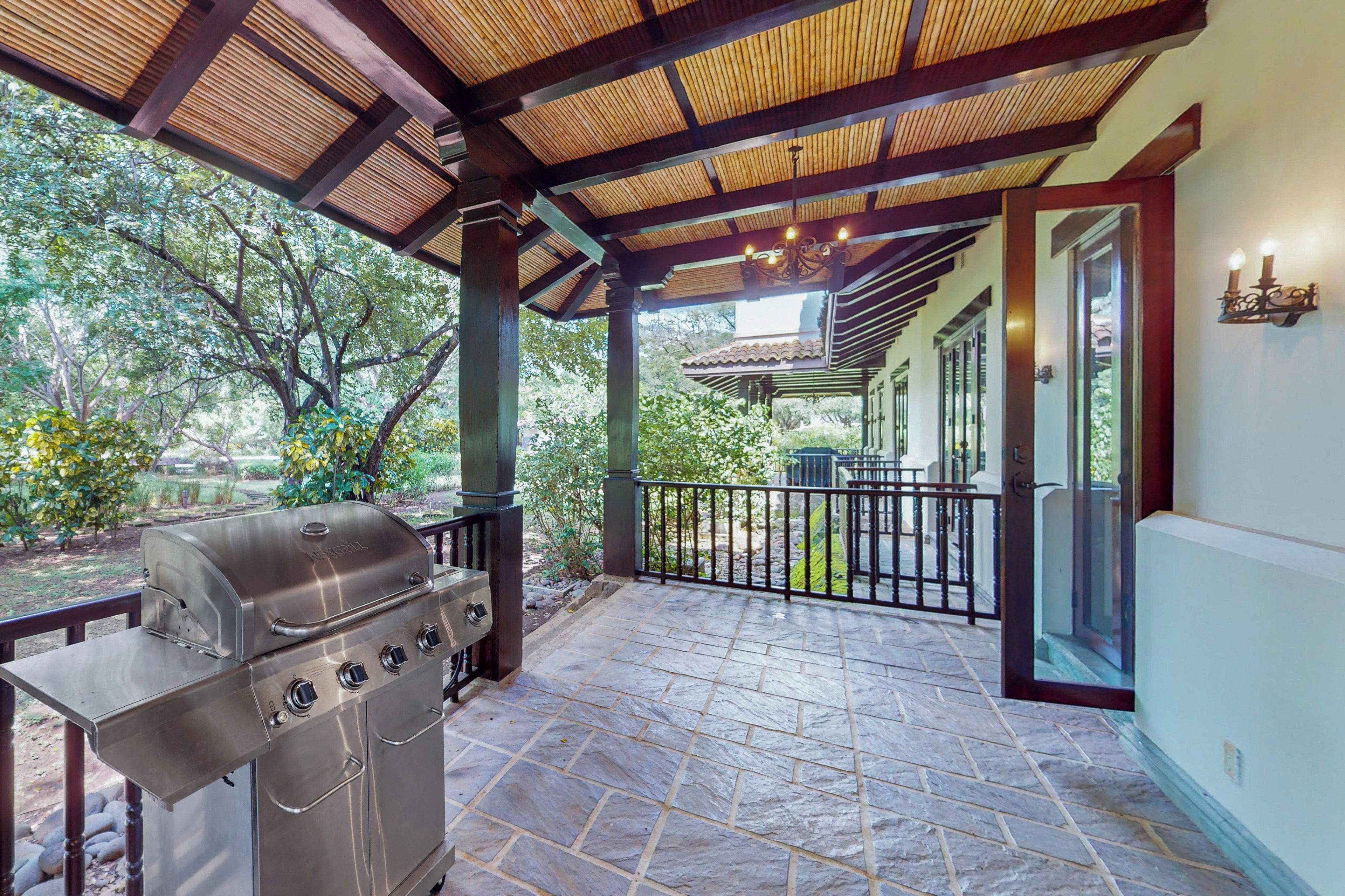 Un espacio exterior cubierto con una parrilla, suelo de piedra y vistas a un jardín.
