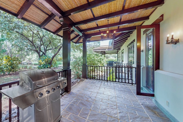 A covered outdoor area with a barbecue grill, stone flooring, and a view of a garden.
