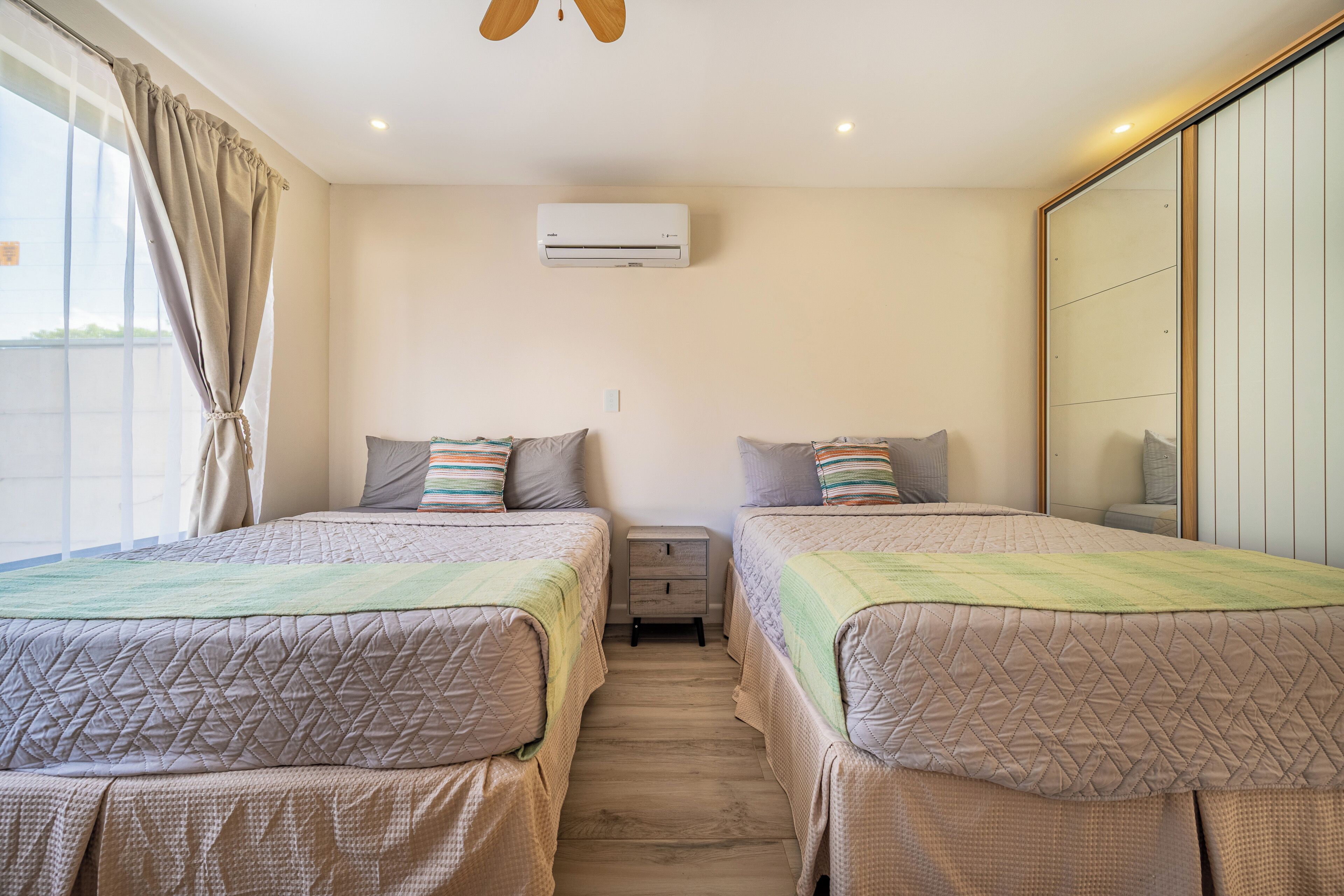 A bedroom with two beds, a wardrobe, a ceiling fan, and an air conditioning unit.