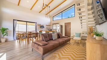 A modern living room with a brown sofa, wooden flooring, and a large window.