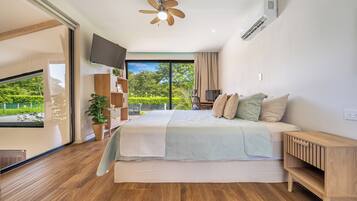 Ein Schlafzimmer mit einem Bett, einem Fernseher, einem Deckenventilator und Blick auf Grünfläche.