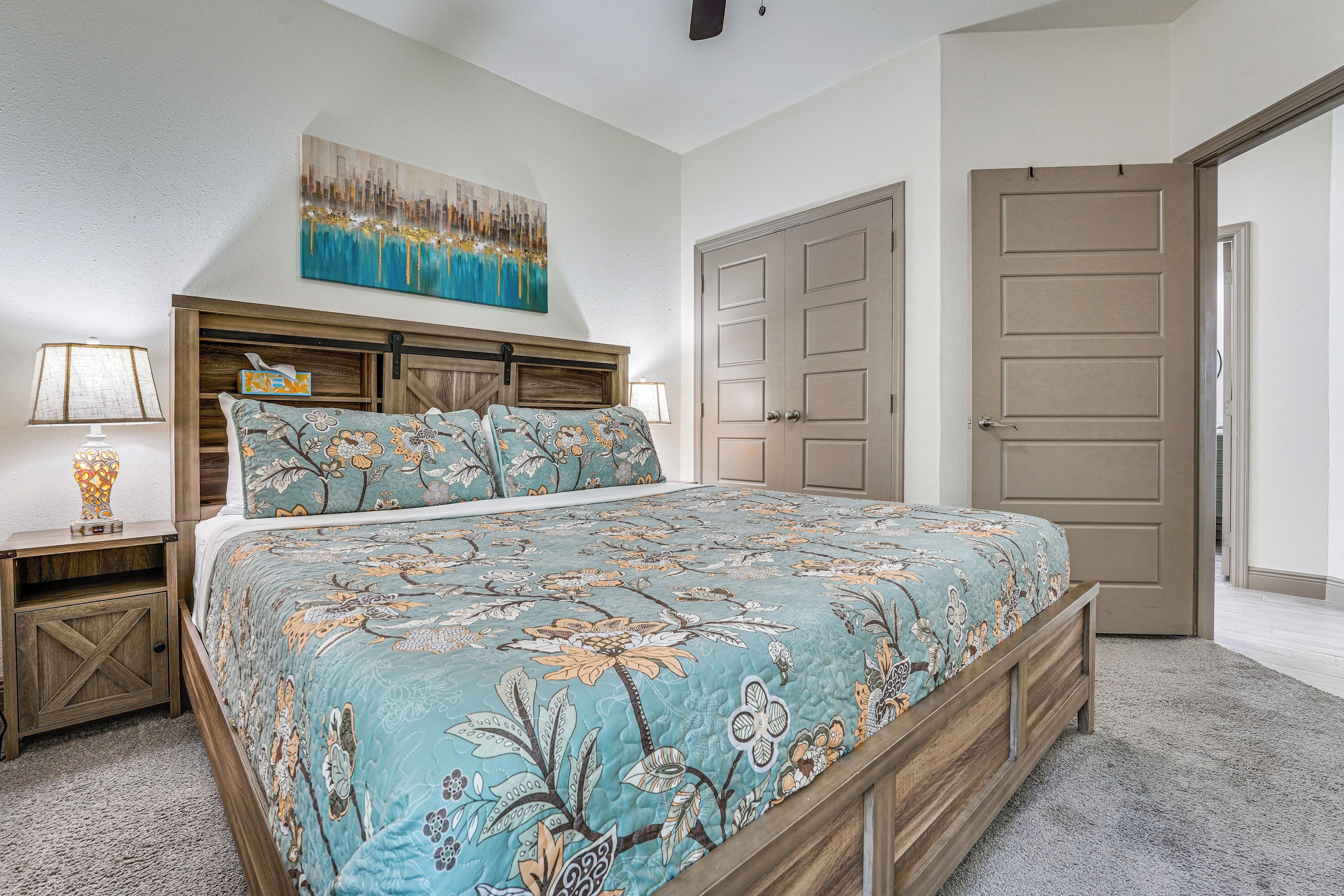 A bedroom with a bed, nightstands, a painting, and a door.