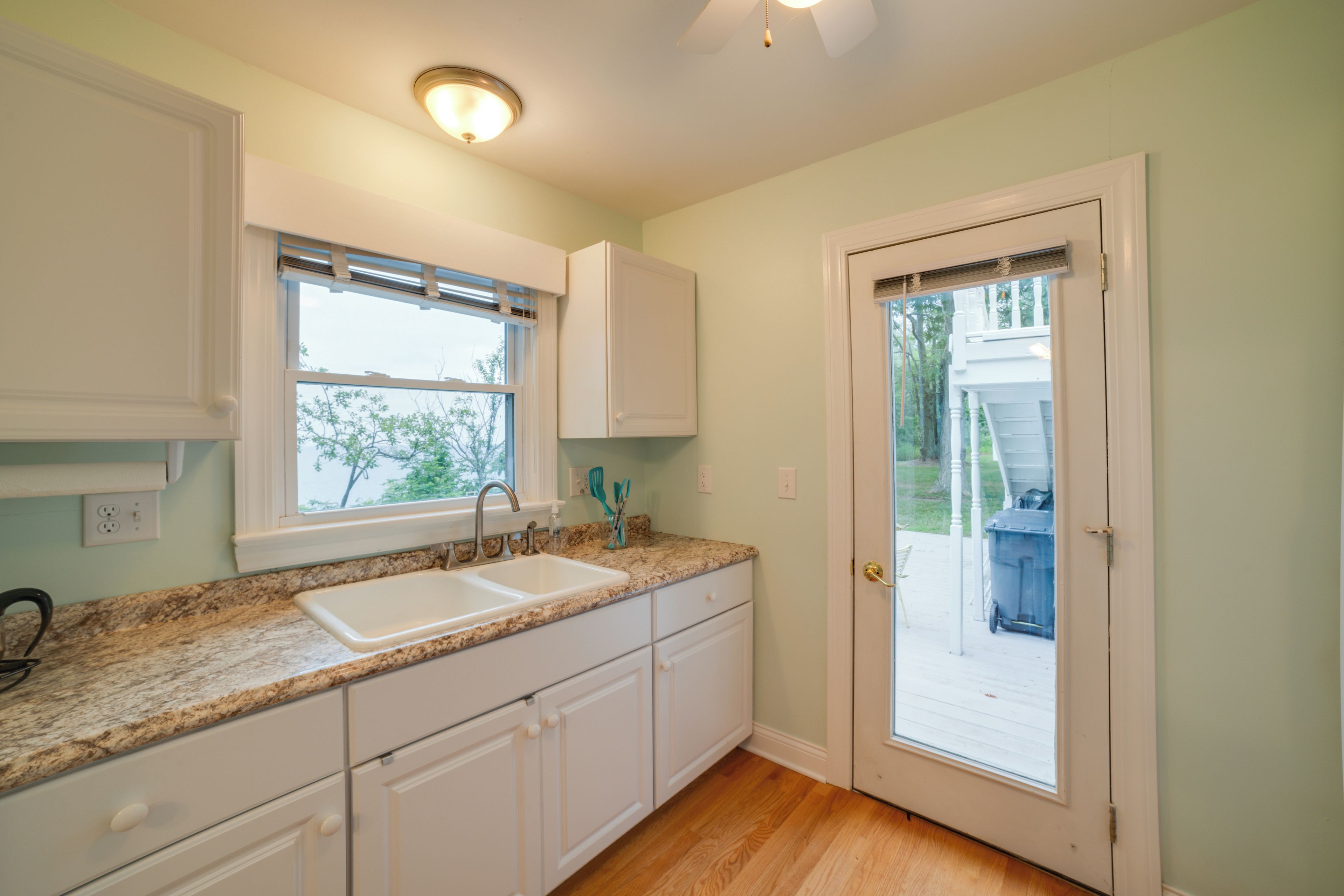 A kitchen with white cabinets, a double sink, and a window with blinds.
