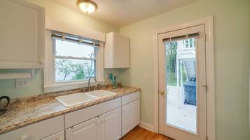 A kitchen with white cabinets, a double sink, and a window with blinds.