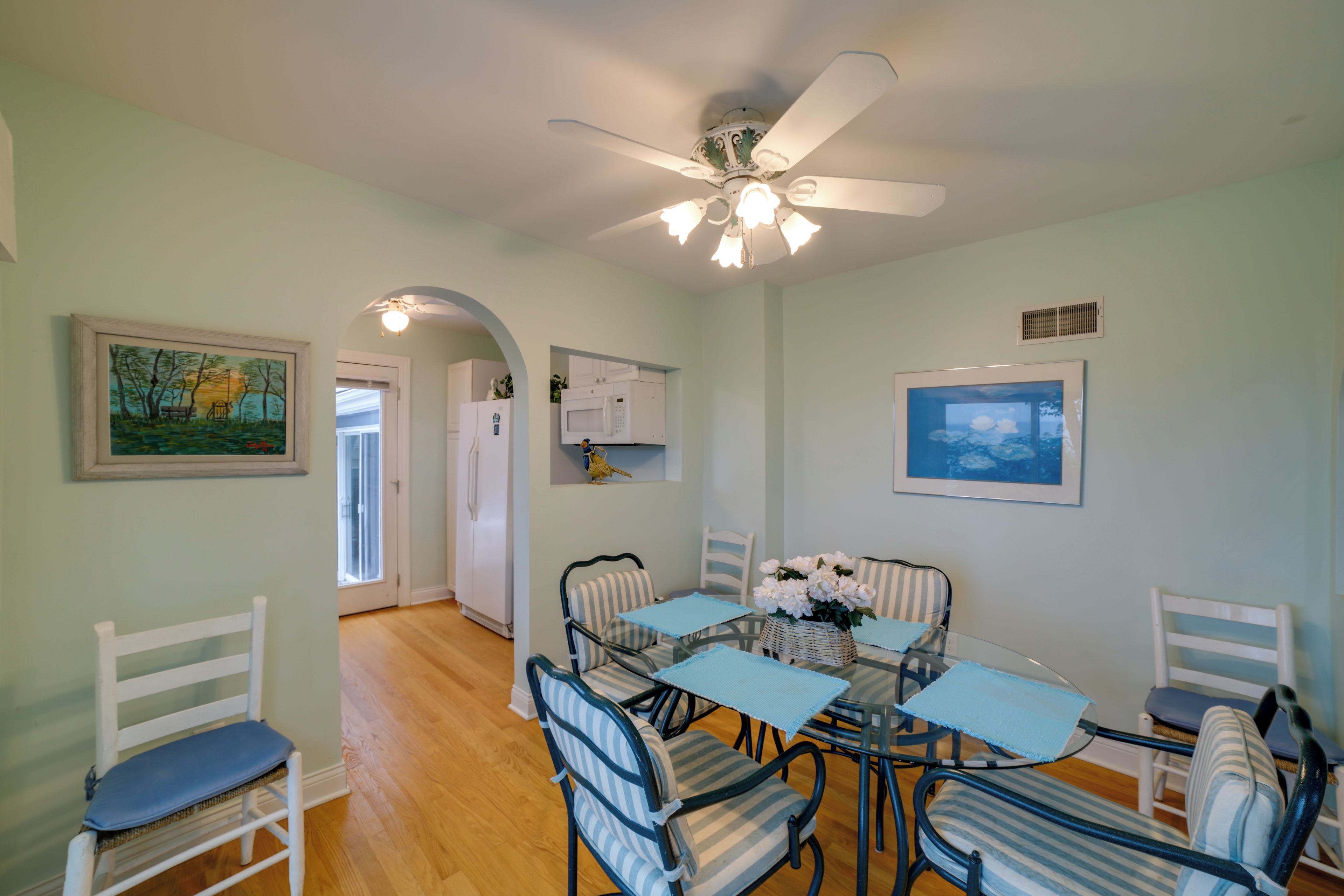 A dining area with a ceiling fan, a table with chairs, and artwork on the walls.