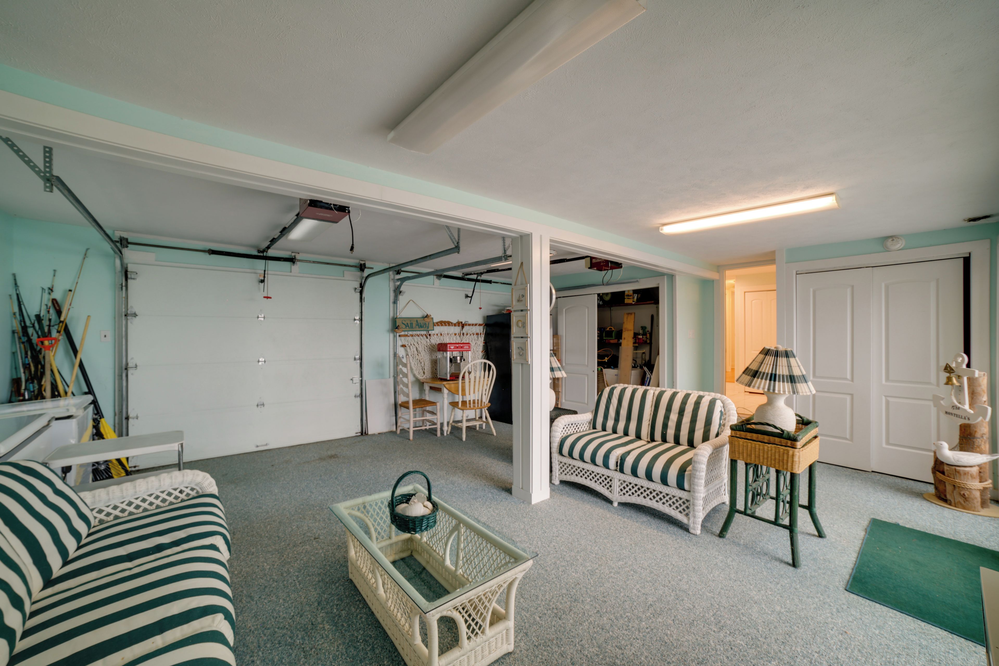 A spacious garage with a white door, a wicker sofa, and a small table with a lamp.