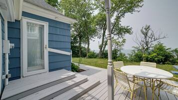 A deck with a white table and chairs, a blue house, and a view of trees and sky.