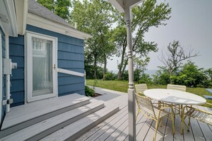A deck with a white table and chairs, a blue house, and a view of trees and sky. - Lakefront Apt w/ Sweeping Views in St Joseph (Saint Joseph)