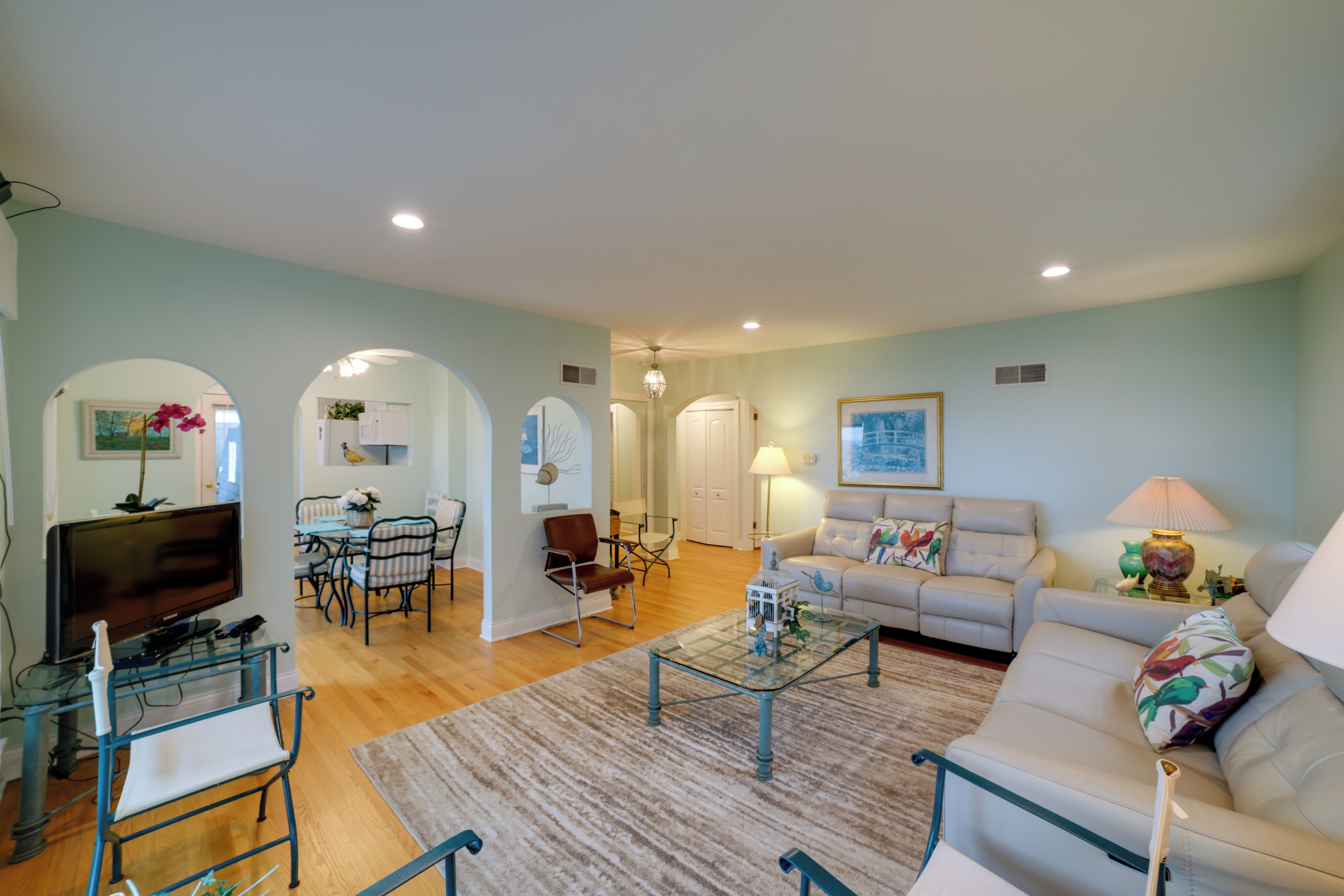 A spacious living room with a sofa, coffee table, and a television. There is a dining area with chairs and a table.