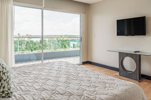A bedroom with a large bed, a TV mounted on the wall, and a balcony with a view of greenery and water. - El Roble Marina, Pool & Estuary Views (Puntarenas)