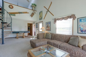 A living room with a pool table, a sofa, a glass coffee table, and a staircase.