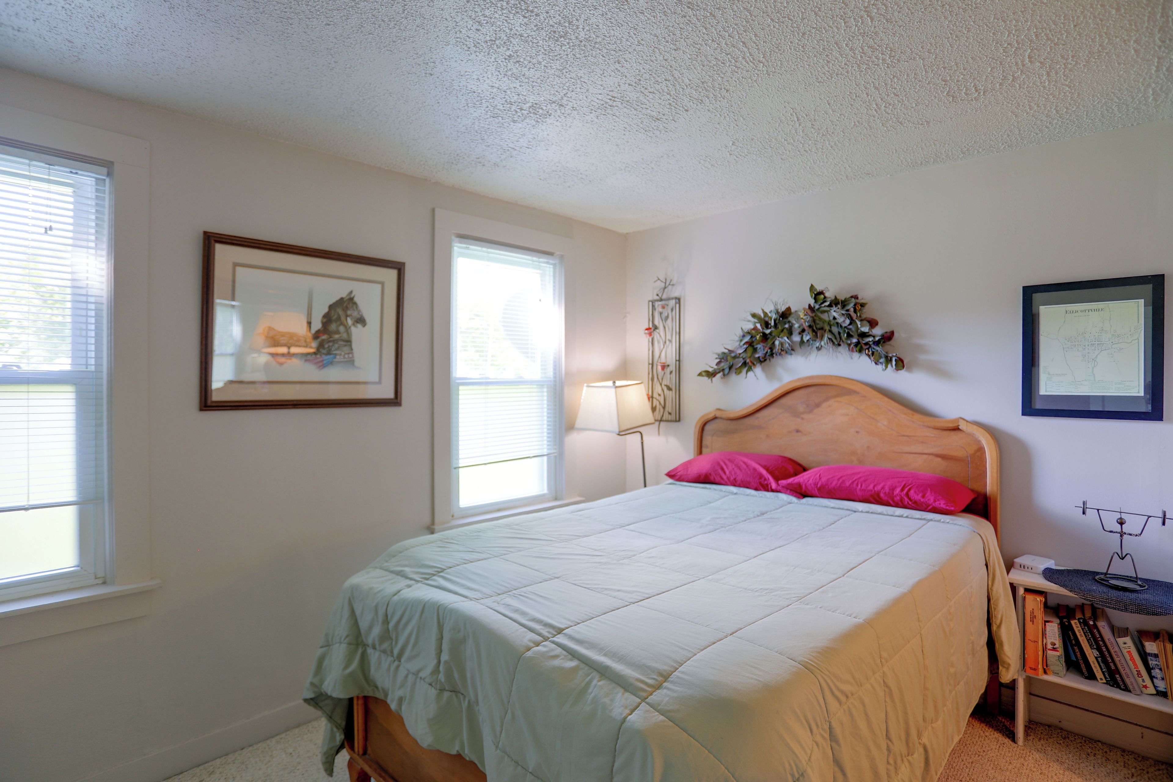A bedroom with a bed, a nightstand, a lamp, and a wall-mounted shelf with books.