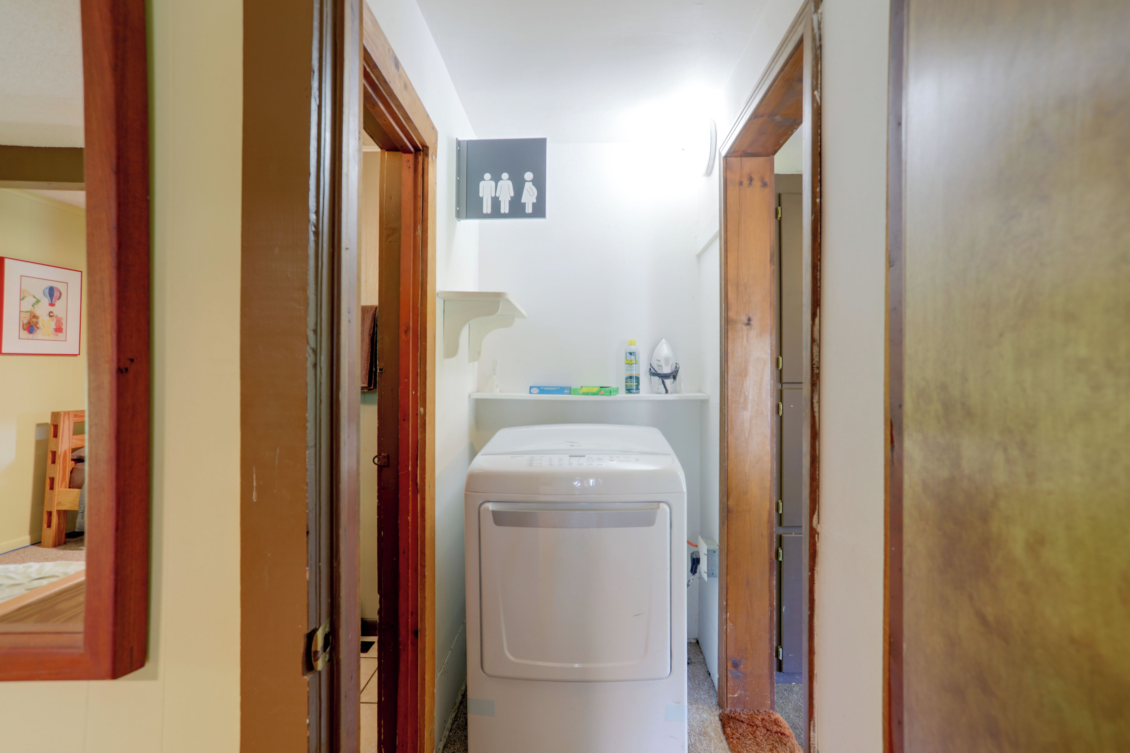 A laundry room with a washing machine, a shelf with cleaning supplies, and a door with a sign indicating a men's restroom.