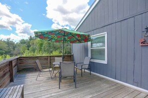 A covered outdoor deck with a table and chairs, a colorful umbrella, and a building with a window and a sign.