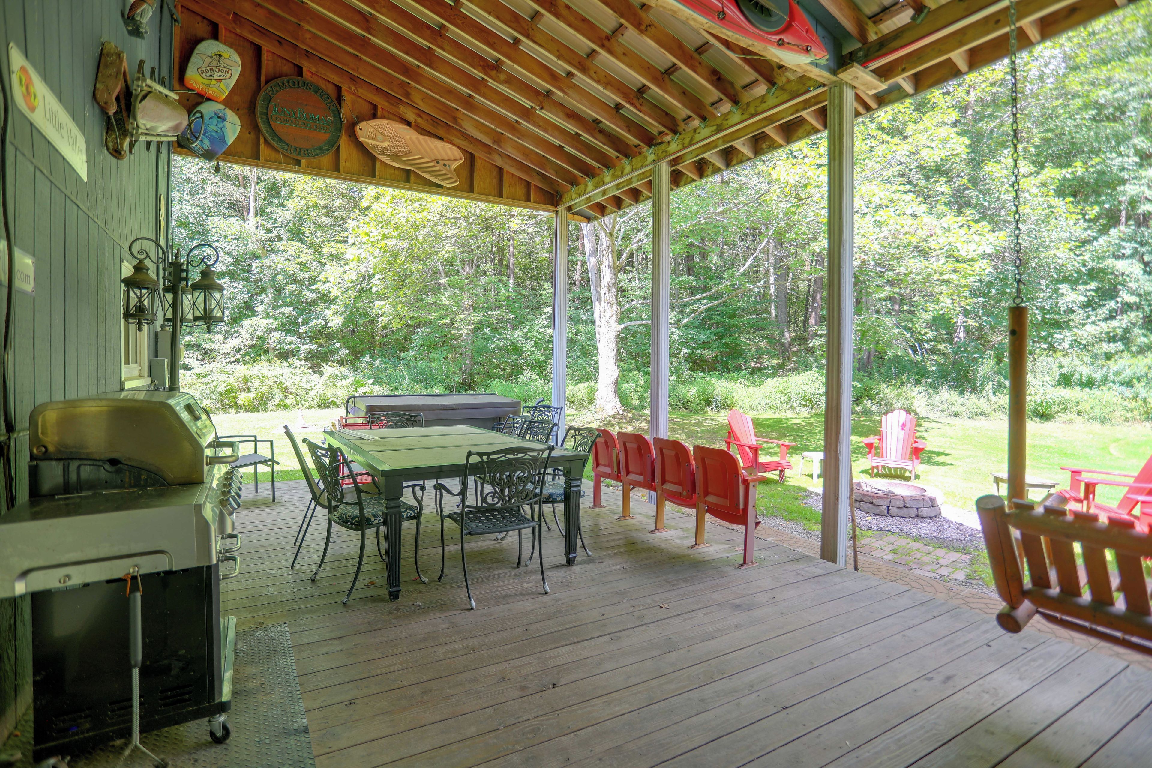 Een overdekt terras buiten met een barbecue, eettafel en stoelen.