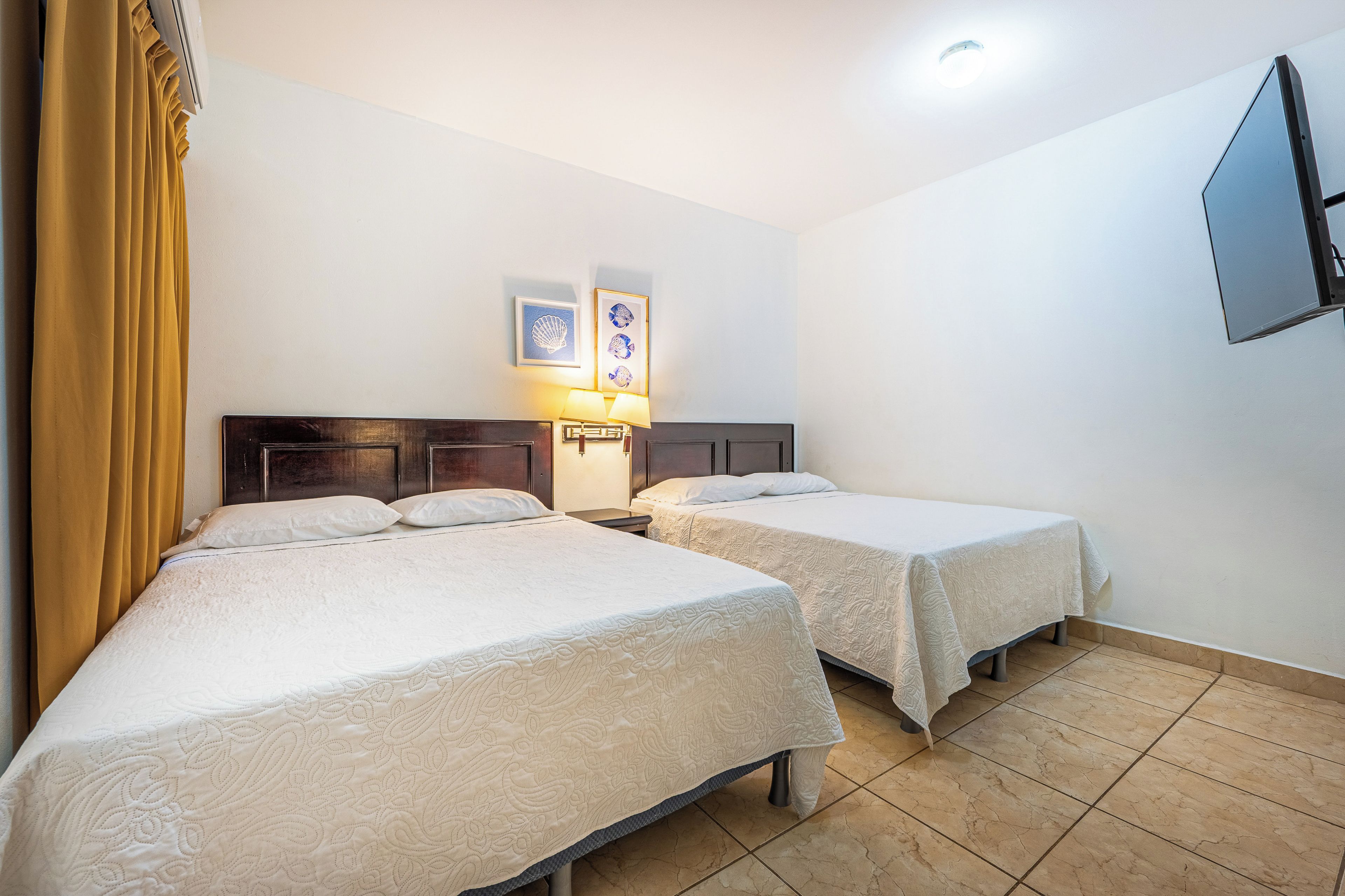 Ein Hotelzimmer mit zwei Betten, einem Nachttisch, einem an der Wand montierten Fernseher und einer Deckenleuchte.