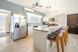 Una cuina moderna amb una illa central, electrodomèstics d'acer inoxidable i un ventilador de sostre.