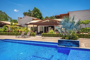 Una piscina con sillas de descanso, un porche cubierto y un jardín ajardinado con diversas plantas.