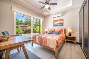 Un dormitorio con cama, mesitas de noche, un escritorio y vistas al exterior.