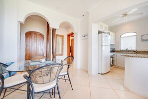 Een moderne keuken met een inbouwkoelkast, een eethoek met een glazen tafel en rieten stoelen, en een plafondventilator.