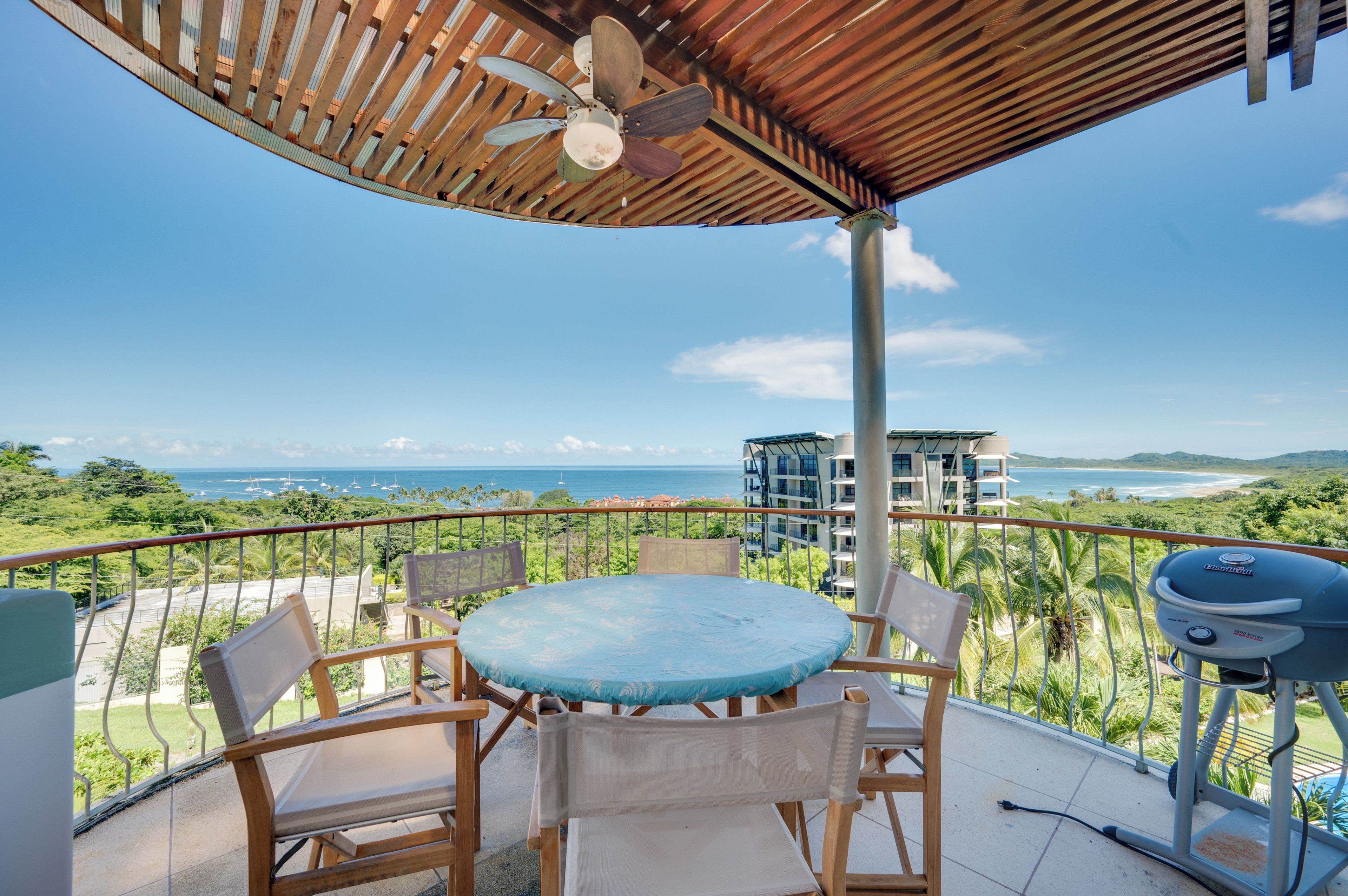 Un balcon avec une table ronde et des chaises, un ventilateur de plafond et un barbecue.
