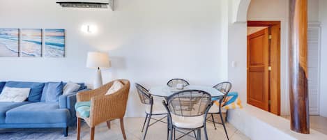 Ein Wohnzimmer mit einem blauen Sofa, einem Esstisch mit Stühlen und einer Wand-Klimaanlage.