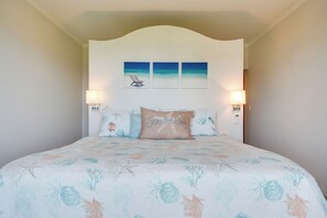 Een slaapkamer met een bed, twee wandlampen, een hoofdeinde met een strandthema schilderij en een kussen met de tekst 'Seas the Day'.