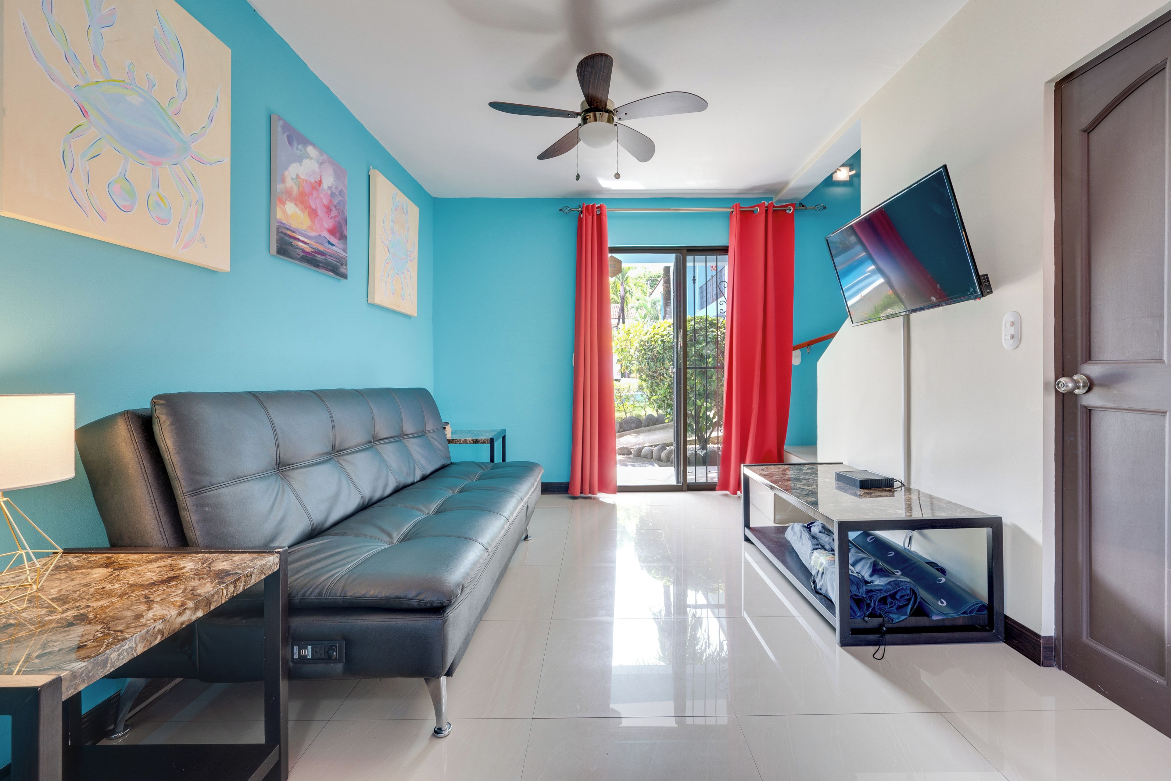 Ein modernes Wohnzimmer mit einem schwarzen Ledersofa, einem Marmor-Couchtisch, einem Deckenventilator und einem an der Wand befestigten Fernseher.
