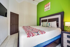 A hotel room with a bed, a nightstand, a lamp, a television, and a green wall. - Playas del Coco: Pool & Private Terrace (Sardinal)