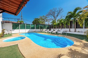A swimming pool with a sandy edge, surrounded by white lounge chairs and palm trees. - Playas del Coco Condo w/ Pool: Walk to Beach! (Sardinal)
