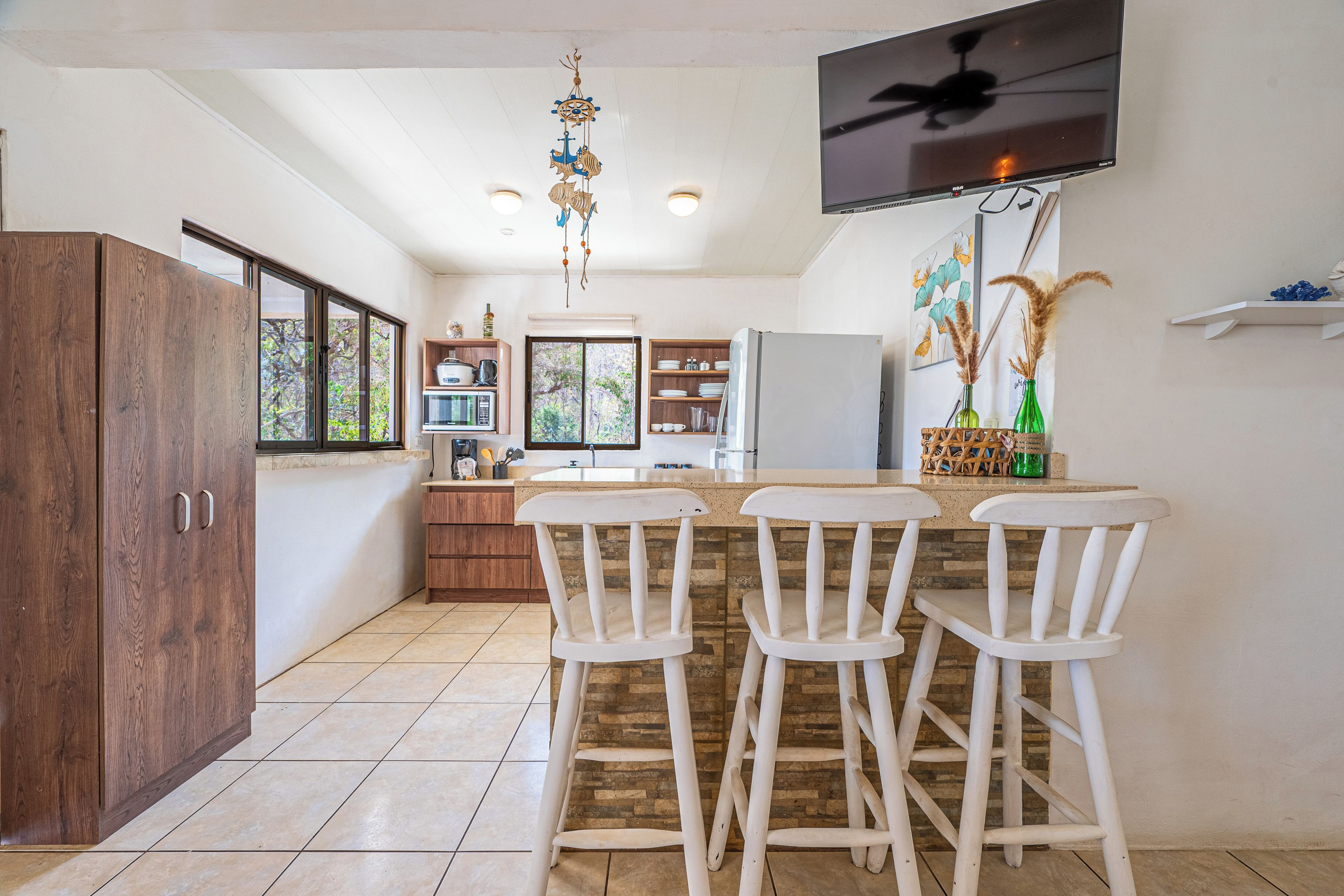 Une cuisine avec un coin bar, des meubles en bois, un téléviseur fixé au mur et un objet décoratif suspendu.