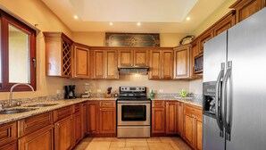 A kitchen with wooden cabinets, stainless steel appliances, a granite countertop, and a tiled floor. - Near Lake Arenal & Volcano: Duplex Unit w/ Views! (Tronadora)