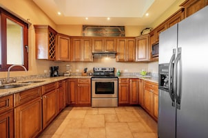 Una cocina con gabinetes de madera, electrodomésticos de acero inoxidable, encimera de granito y piso de baldosas.
