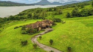 A rural house with a thatched roof surrounded by lush greenery and a winding path leading to it. - Near Lake Arenal & Volcano: Duplex Unit w/ Views! (Tronadora)