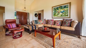 A living room with a sofa, armchair, and coffee table. There is a painting on the wall and a door leading to another room. - Near Lake Arenal & Volcano: Duplex Unit w/ Views! (Tronadora)