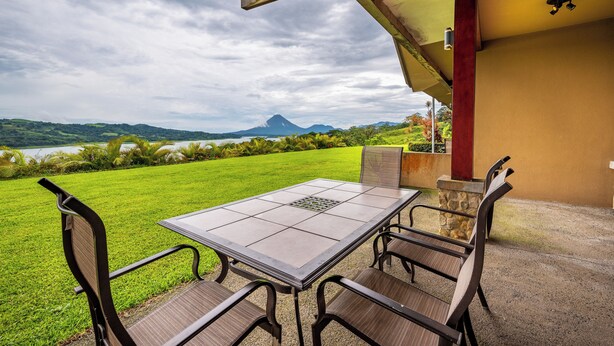An outdoor patio with a table and chairs, overlooking a grassy area with a mountain in the distance. - Near Lake Arenal & Volcano: Duplex Unit w/ Views! (Tronadora)