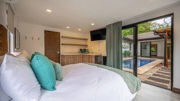 A bedroom with a large bed, a built-in kitchen, and a sliding glass door leading to a pool area.