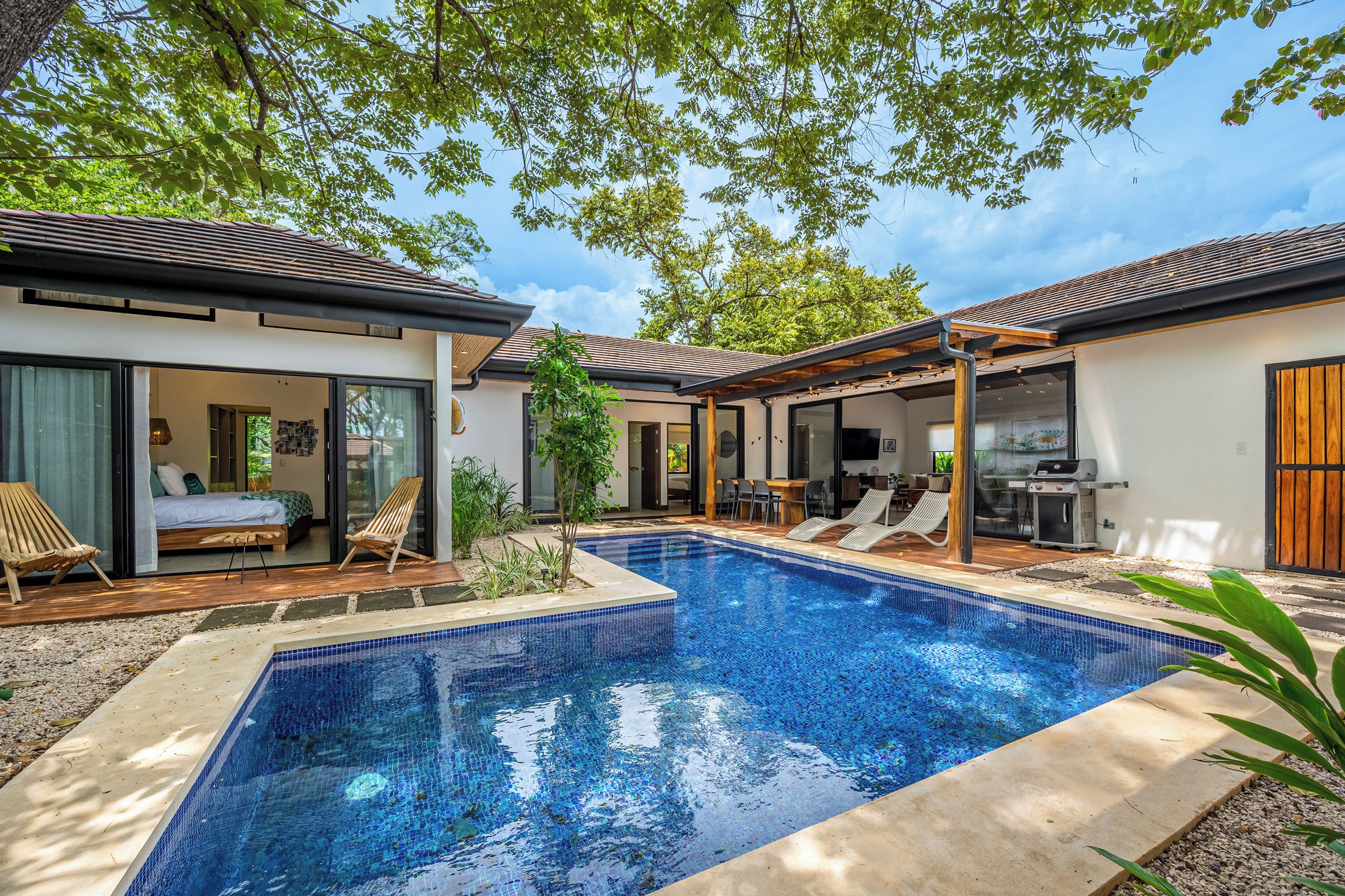 A modern outdoor pool area with a clear blue pool, wooden deck, and lounge chairs.