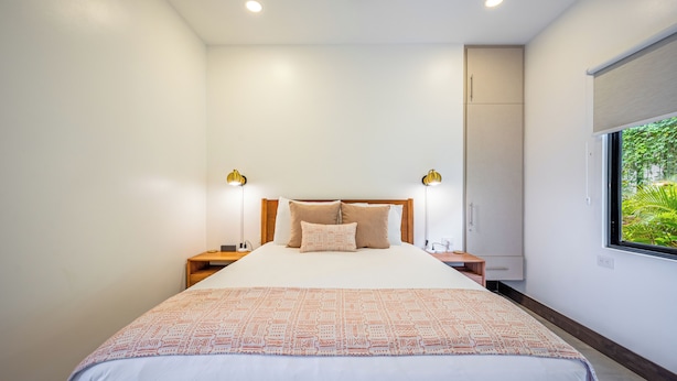 A modern bedroom with a large bed, bedside lamps, a wardrobe, and a window with a view of greenery. - Modern 4BR Family Home w/ Pool in Tamarindo (Tamarindo)