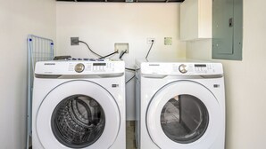 Two white Samsung washing machines in a laundry room with a metal rack and a wall-mounted electrical outlet. - Modern 4BR Family Home w/ Pool in Tamarindo (Tamarindo)