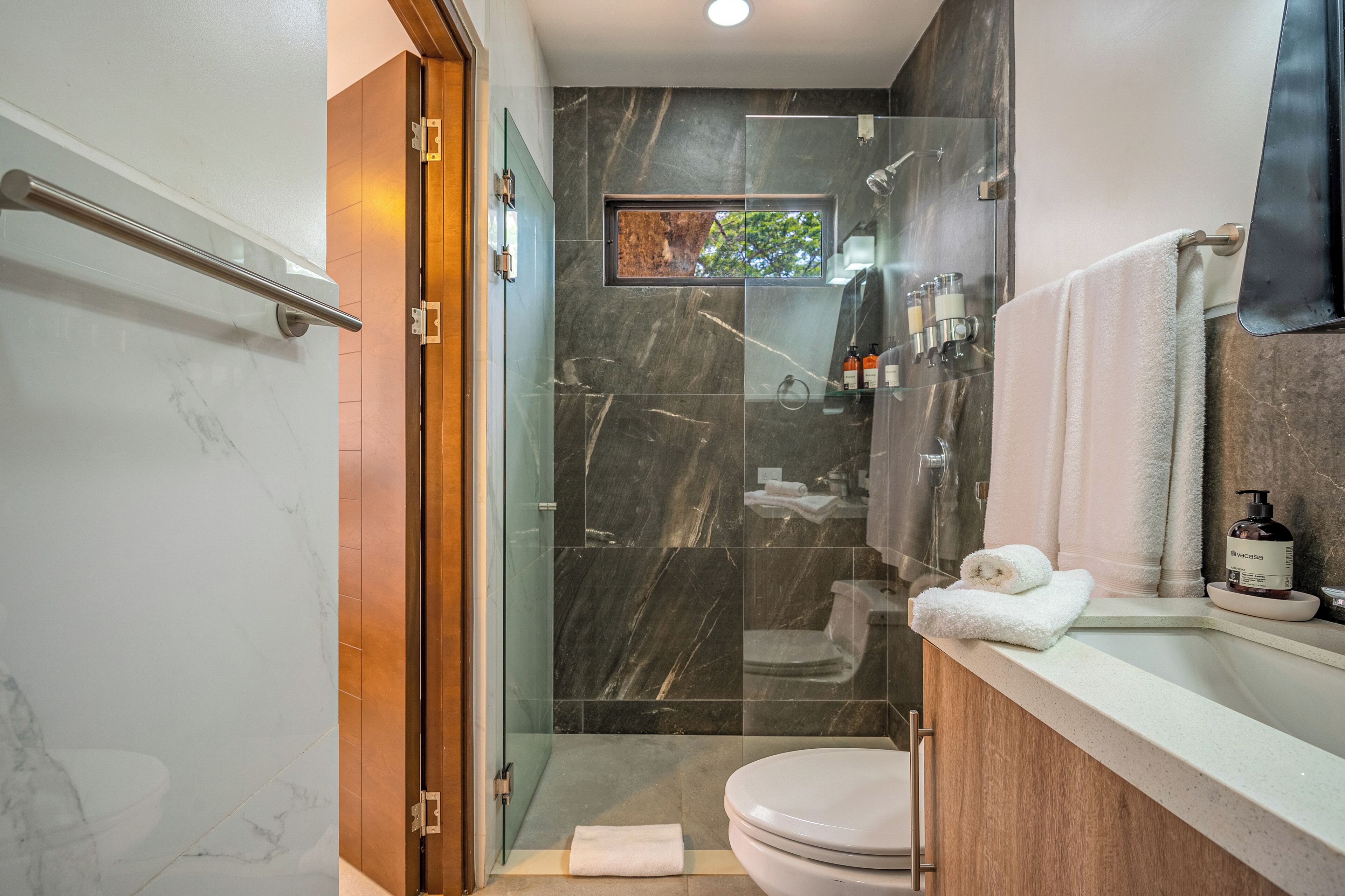 A modern bathroom with a glass-enclosed shower, a toilet, and a vanity with toiletries.