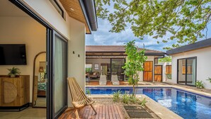 A modern outdoor pool area with a wooden deck, a small tree, and a view of the interior living space. - Modern 4BR Family Home w/ Pool in Tamarindo (Tamarindo)