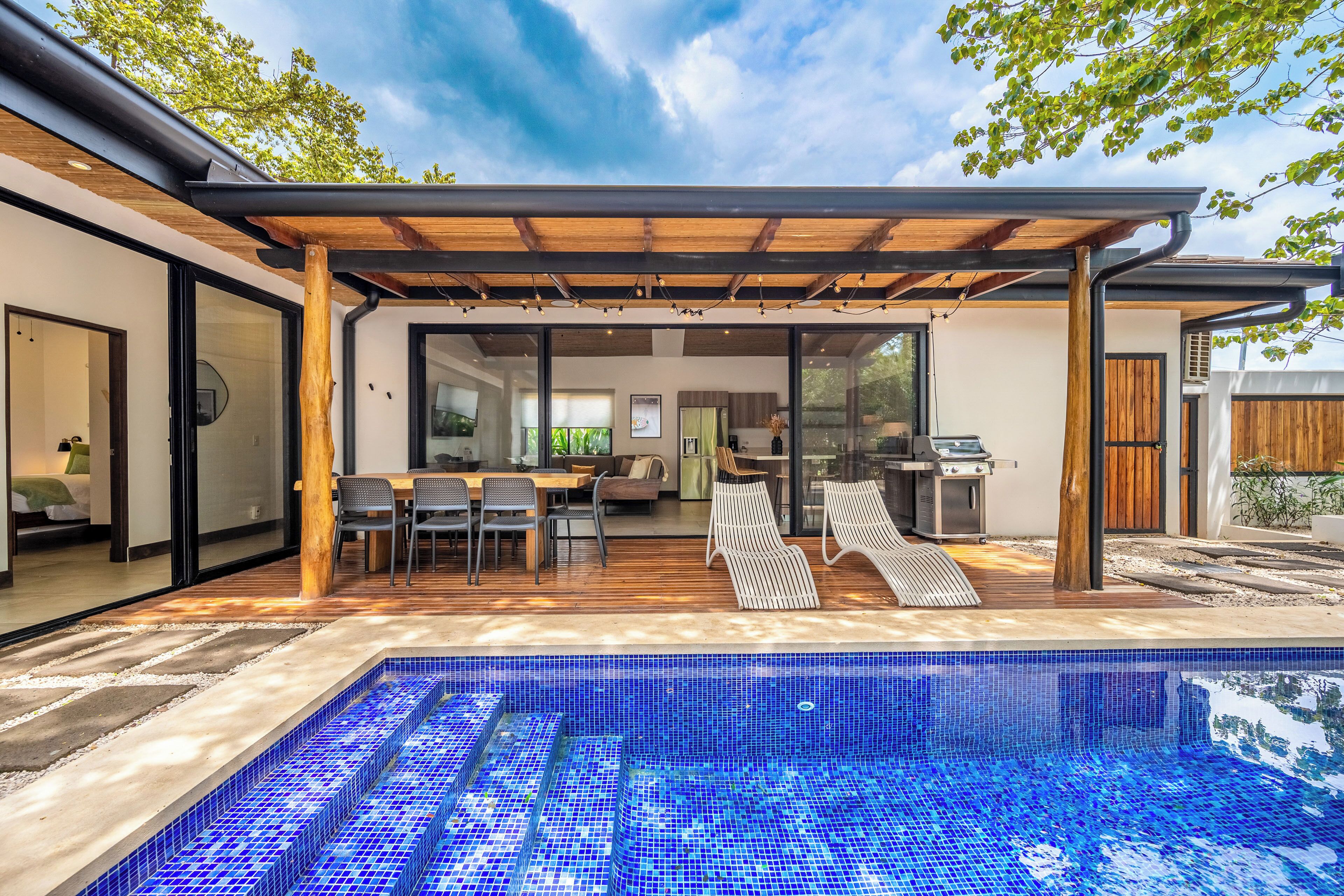 A modern outdoor pool area with a pergola, dining space, and a barbecue grill.
