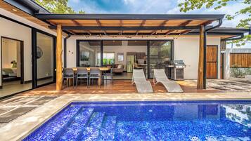 A modern outdoor pool area with a pergola, dining space, and a barbecue grill.