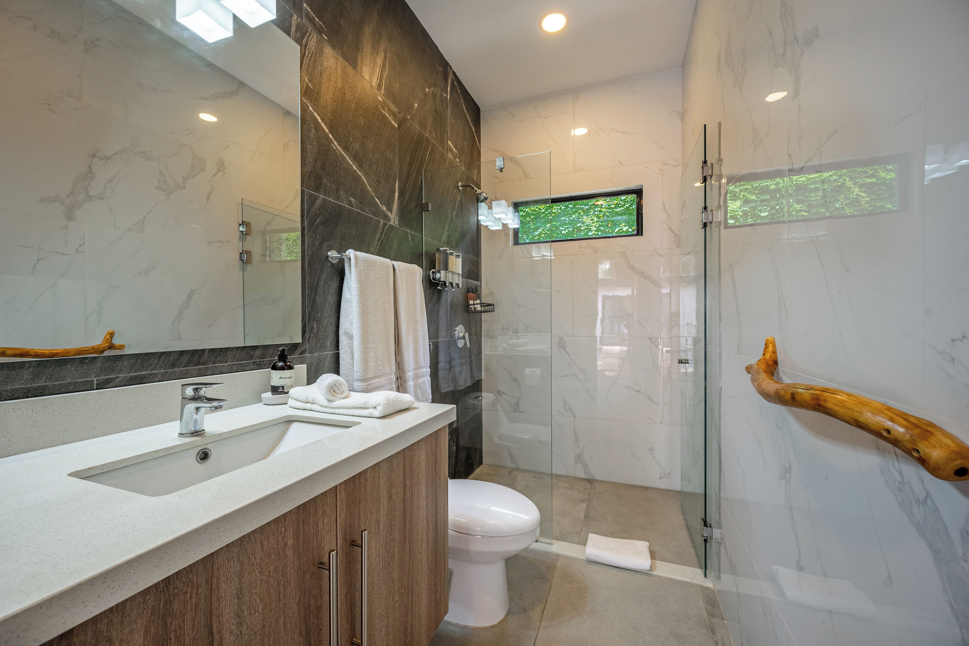 A modern bathroom with a marble vanity, a glass shower enclosure, and a mounted television.