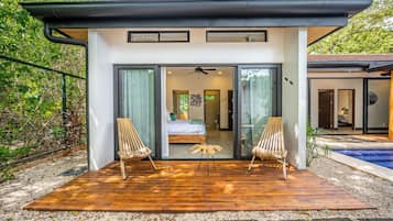 A modern house with a wooden deck, two wooden chairs, and a glass door leading to a bedroom.